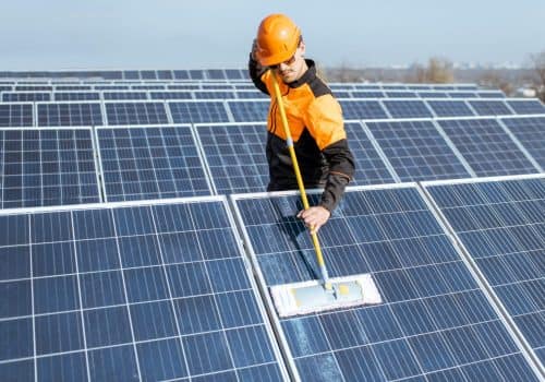 Professional cleaner in protective workwear cleaning solar panels with a mob. Concept of solar power plant cleaning service